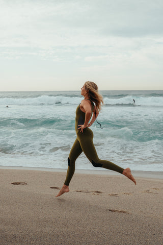 Woman running on a beach with ocean waves in the background wearing long jane